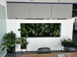 Biuro w stylu Booksy ze ścianą roślin i biurkiem.