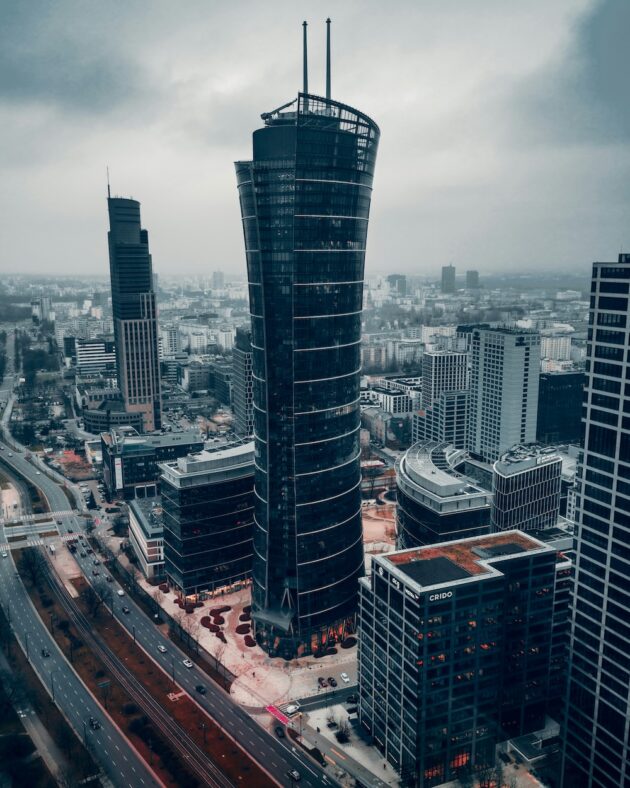 Wysoki, ciemny, nowoczesny wieżowiec stoi wśród innych budynków w miejskim krajobrazie pod zachmurzonym niebem, a kwiaty do biura Warszawa dodają elegancji do tętniącej życiem atmosfery. Wysoki, ciemny, nowoczesny wieżowiec stoi wśród innych budynków w miejskim krajobrazie pod zachmurzonym niebem, a kwiaty do biura Warszawa dodają elegancji do tętniącej życiem atmosfery.