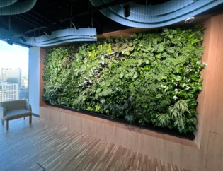 Duża wewnętrzna zielona ściana z różnymi roślinami została zainstalowana na drewnianej ścianie w nowoczesnej przestrzeni biurowej z naturalnym światłem i krzesłem w pobliżu.