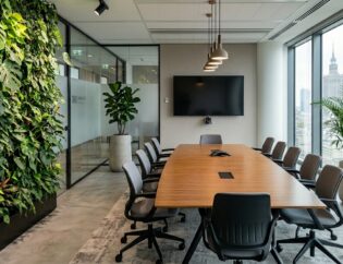 Nowoczesna sala konferencyjna z długim drewnianym stołem, szarymi krzesłami, naściennym ekranem, dużymi oknami i zielonymi roślinami - idealne rośliny do sal konferencyjnych, w tym żywy pionowy ogród na jednej ścianie.