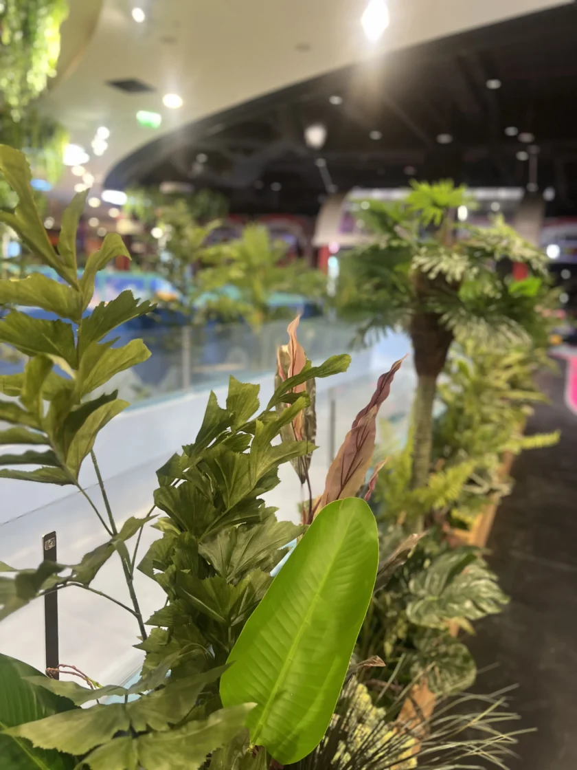 Rośliny domowe i sztuczna zieleń ustawione wzdłuż krawędzi szklanej bariery w dobrze oświetlonej przestrzeni publicznej lub centrum handlowym.