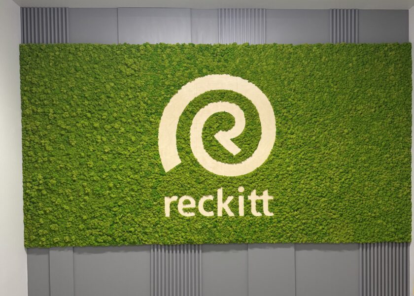 Prostokątna ściana z mchu w kolorze zielonym z logo i nazwą Reckitt w kolorze białym, zamontowana na szarym tle.