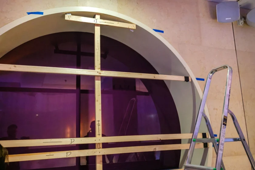 Duże okno łukowe otoczone drewnianą ramą, a po prawej stronie stoi metalowa drabinka. Duże okno łukowe otoczone drewnianą ramą, a po prawej stronie stoi metalowa drabinka.